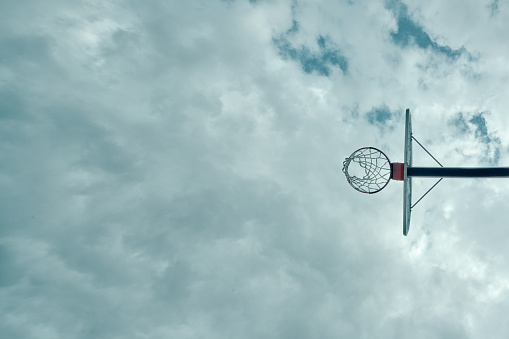 Basketball hoop high in the sky during the daytime with clouds in background.