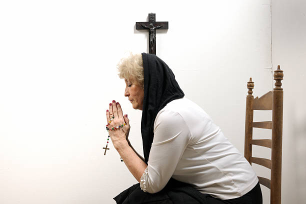 Elderly Asian woman seeming to pray with hands clasped together.