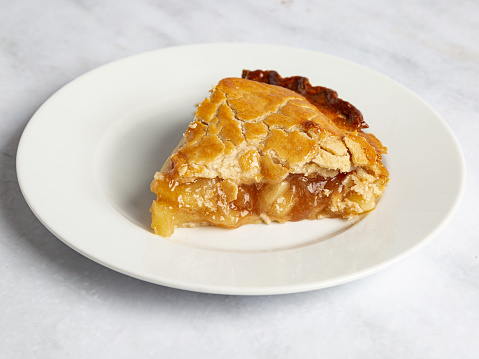 Hot out of the oven home made apple pie, a slice or in the pan with a lifestyle environment. Props wood utensil, silver fork, white serving plate, cloth towel, on a wood or marble surface.