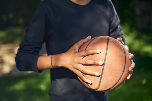 A young adult holds the basketball, ready for his opportunity at a pickup basketball game at the park
