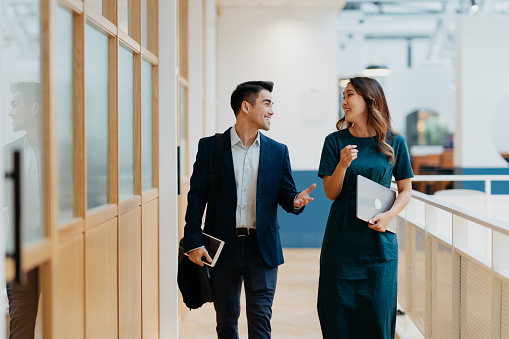 Image of two white collar workers having a discussion in modern office. Businessman and businesswoman discussing business strategy while walking in the corridor