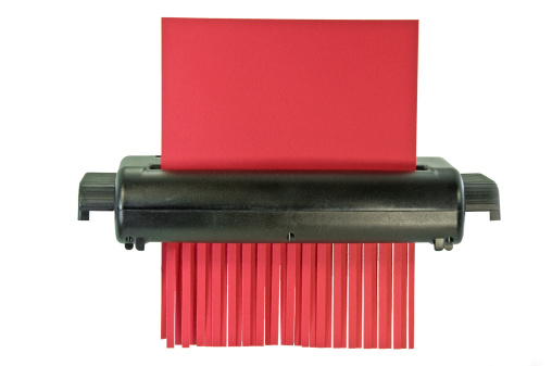 A paper shredder with a piece of red  paper half shredded. Clipping path
