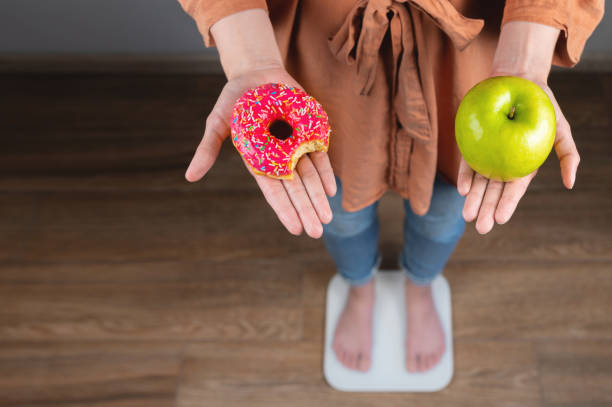 It's hard to choose a healthy food concept when a woman holds a green apple and a donut with a high-calorie dessert in her hand stock photo