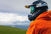 Portrait of an unrecognizable male cyclist against the backdrop of clouds and mountains. a man in a full-face helmet with chin protection and mirrored goggles mask looks away
