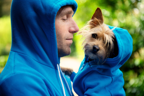Young man holding his best friend dog in matching blue hoodies in bright green park background outdoors