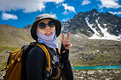 hipster shows tongue, funny face, posing in the countryside on a sunny day, stylish hat and sunglasses. woman with a backpack on a hike rejoices