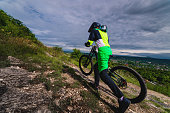 mountain biker carries a bicycle in a forested landscape of summer mountains. MTB track for cycling. Outdoor sports, the guy carries the bike to the top