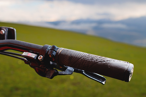 Close-up of a mountain bike handle against the background of green meadows of mountains and clouds.