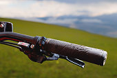 Close-up of a mountain bike handle against the background of green meadows of mountains and clouds