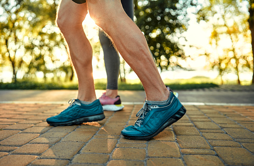 Morning walk on nature. Crop of athletic male person in blue sneakers walking on cobblestone pavement in park together with woman. Active couple leisurely strolling outdoors and breathing fresh air.
