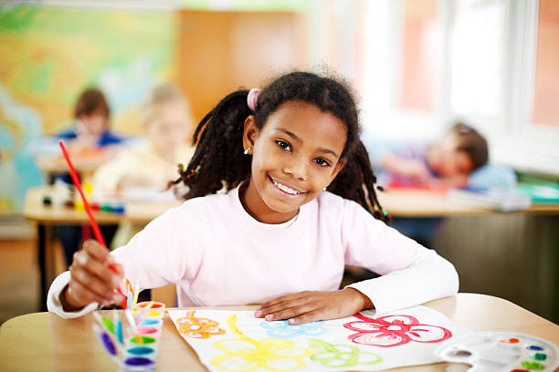 Cute African-American girl is painting with watercolors. Smiling African ethnic schoolgirl is at the Art class drawing with watercolors. She is looking at the camera.    art class photos stock pictures, royalty-free photos & images