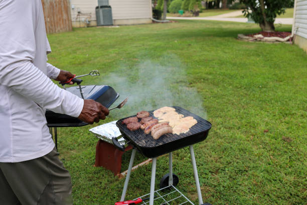 A black man grilling meat on a charcoal grill in a backyard