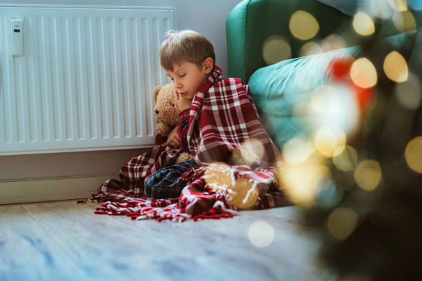 istock cute little boy wrapped id plaid sitting by heater 1700563788
