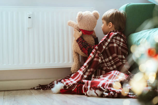 istock cute little boy wrapped id plaid sitting by heater warming teddy bear paws 1700564322