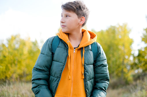 Portrait cheerful teen walking school at autumn. Boy is in a yellow looking camera