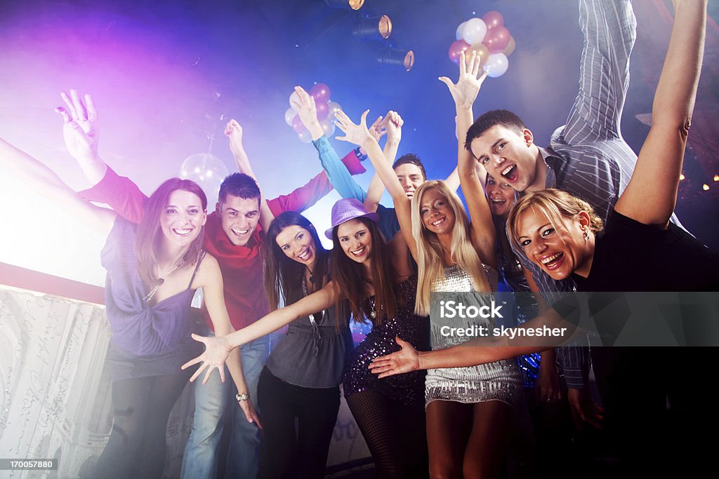 Group of young people with arms raised at a club Large group of smiling cheerful friends with raised arms are looking at the camera at the disco club.    Celebration Stock Photo