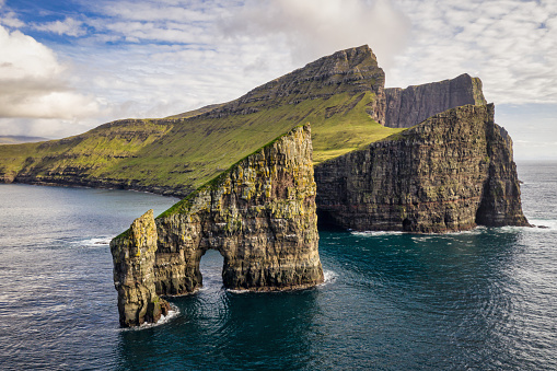 Faroe Islands, the famous Drangarnir Rocks in the North Atlantic Ocean in sunny summer. Aerial Drone Point of view, Beautiful warm late afternoon light and summer cloudscape, The Drangarnir Rocks are located between the Islet Tindholmur and Vágar Island on the southside of Sørvágsfjørður. Faroe Islands, Denmark, Nordic Countries, Europe