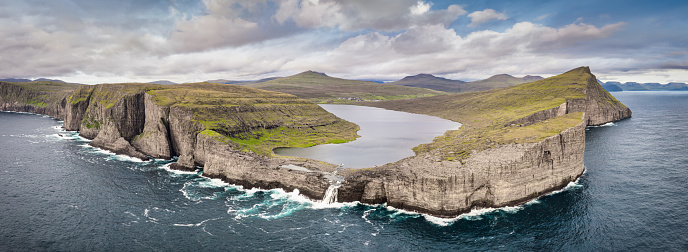 Faroe Islands XXL Panorama of Sørvágsvatn Lake - Leitisvatn - Sorvagsvatn is the largest lake in the Faroe Islands, above the Atlantic Ocean. Aerial Drone XXL Panorama towards the rocky coastline of Vagar - Vágar Island, Bosdalafossur Waterfall and Trælanípa Slave Cliff. Sørvágsvatn lake surface is about 40 metres above the level of sea., surrounded by higher cliffs preventing it from emptying fully into the ocean, the waterfall Bøsdalafossur being the lake outlet. Vágar Island, Faroe Islands, Denmark, Nordic Countries, Europe