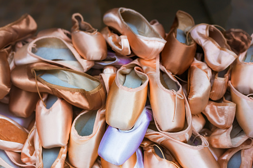 Close up image depicting a pile of ballet shoes stacked on top of one another.