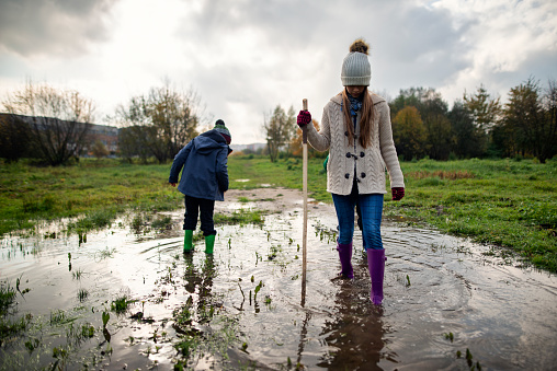 Three kids aged 10 and 6 are playing on autumn day. Kids wearing galoshes are walking through big puddle.\nShot with Nikon D800