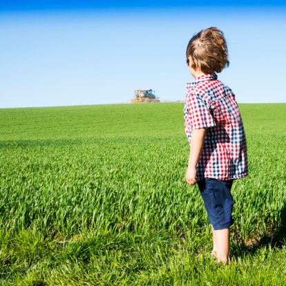 Boy on a farm watching a crop sprayer in a hay field.