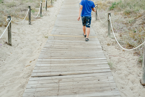 Children walking on wooden path towards the beach in summer