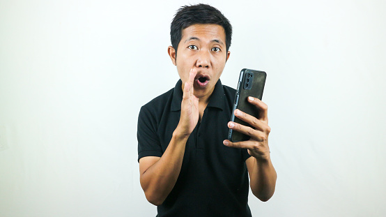 Asian man hold smartphone and whispering some secret gossip isolated on white background.