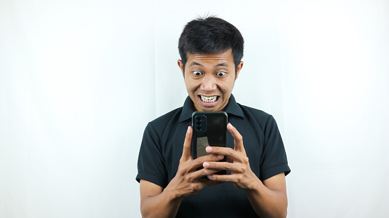 Disappointed, not expect, angry expression of asian man reading bad news at mobile phone isolated on white background.