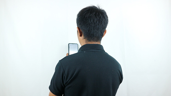 Back of view of a man typing a message on his phone. Back view of people collection. behind people. Isolated over white background. The man in the black t-shirt.