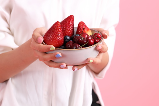 The Asian woman holding berry fruit in the hand on the pink background.