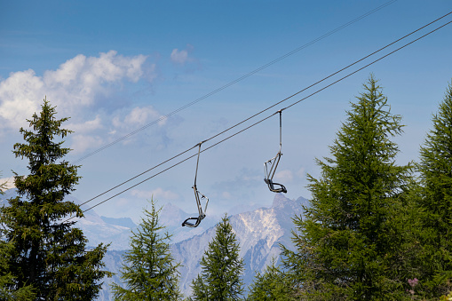 An empty ski chair lift in the summer, above the forest, with mountains in the background. Ski resort La Fouly in Switzerland. Copy space above.