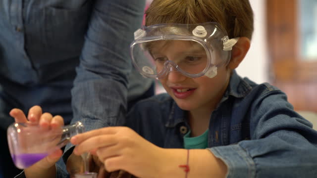 Unrecognizable teacher helping a happy little boy during science class mix some liquids