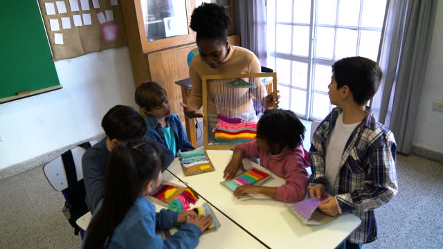Black woman teaching her students how to hand weave during arts and crafts class at school