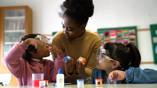 Cheerful black teacher talking to her excited students during science class while showing them some chemicals