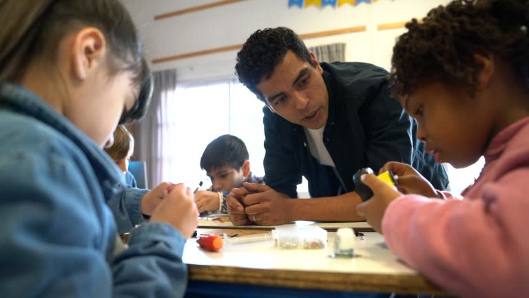 Cheerful teacher talking with black little student asking her questions during robotics class with her friends