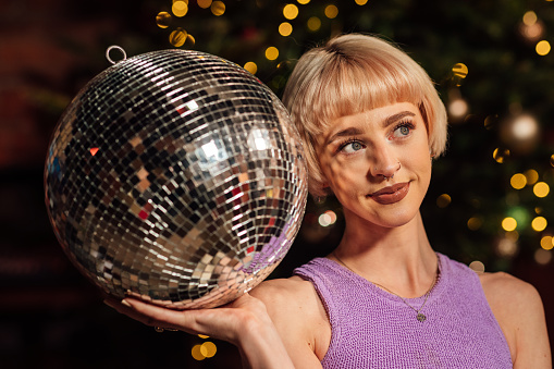 Portrait of a woman at a party in the North East of England. She is looking away from the camera holding a disco ball. There are Christmas lights out of focus behind her.