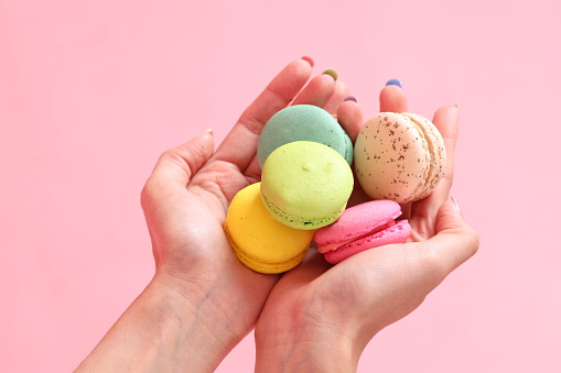 The Asian woman holding macaroons in the hand on the pink background.