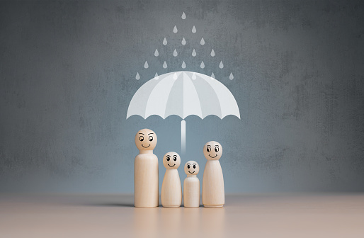Life, House, Car, Business, Travel and Health insurance concepts. Umbrella protecting rain from wooden figures of family members idea for life assurance. Protection against a possible eventuality.