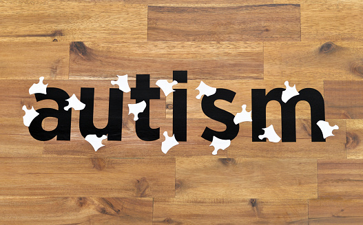 Closeup of the word Autism with puzzle pieces on a wood grain background.