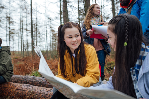 A medium shot of two teenage students on a field trip. They explore nature, blending lessons with the outdoors. They are reading from a map to guide their direction.\n\nVideo also available of this scenario