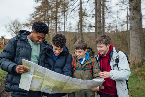 Front view, medium shot of a group of four male student teenagers on an educational walk. They explore nature, blending lessons with the outdoors. They are using a map and navigational equipment to orienteer in the woods.

Video also available of this scenario
