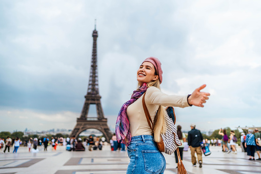 Young happy woman tourist in front of the Eiffel Tower in Paris, France