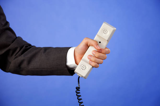 бизнесмен протягивает телефонную трубку на фиолетовом фоне - telephone telephone receiver phone cord telephone line стоковые фото и изображения