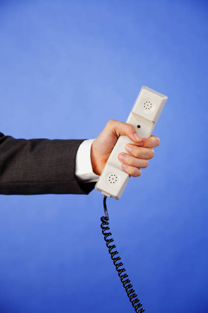 бизнесмен протягивает телефонную трубку на фиолетовом фоне - telephone telephone receiver phone cord telephone line стоковые фото и изображения