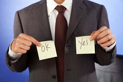 holding up a yellow Post-It note that says, 'YES.' and 'ok'
