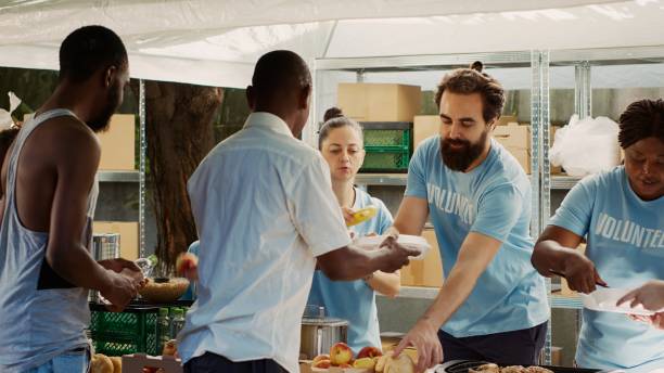 voluntarios sirven comida a desfavorecidos - underprivileged fotografías e imágenes de stock