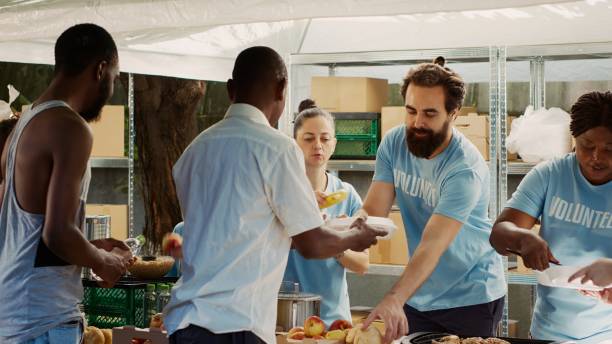 ボランティアは恵まれない人々に食べ物を提供します - underprivileged ストックフォトと画像