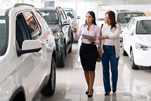 Happy salesperson showing a car to a woman interested in buying a car at the dealership - car ownership concepts