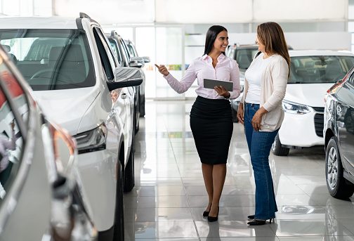 Happy woman buying a car at the dealership and talking to the salesperson - car ownership concepts