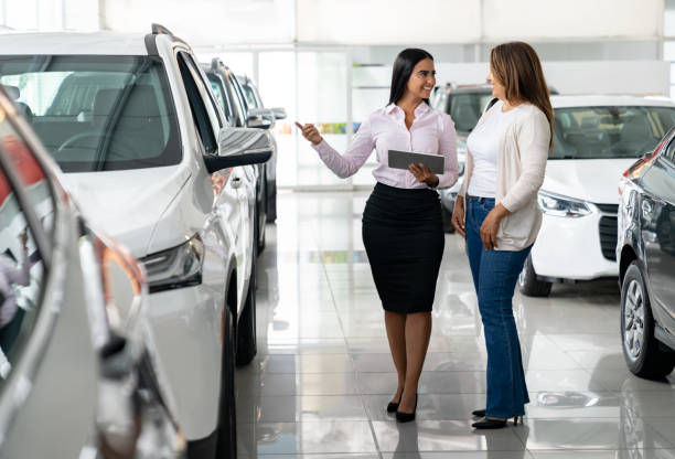 Woman buying a car at the dealership and talking to the salesperson Happy woman buying a car at the dealership and talking to the salesperson - car ownership concepts talking two people business talk business stock pictures, royalty-free photos & images